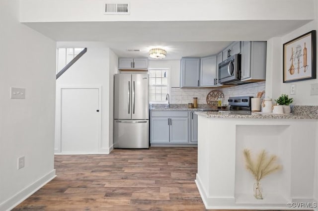 kitchen featuring wood-type flooring, backsplash, gray cabinetry, and appliances with stainless steel finishes