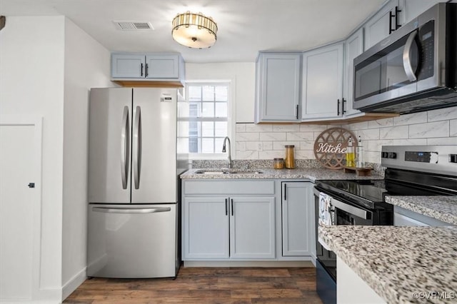 kitchen featuring light stone countertops, dark hardwood / wood-style flooring, stainless steel appliances, sink, and backsplash