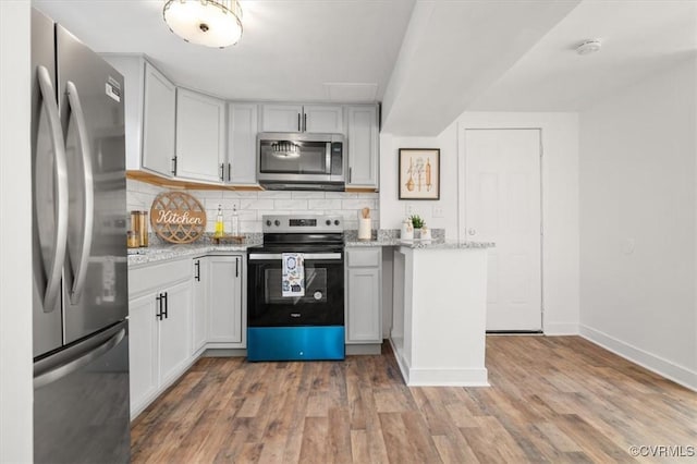 kitchen featuring stainless steel appliances, light stone counters, hardwood / wood-style floors, and tasteful backsplash