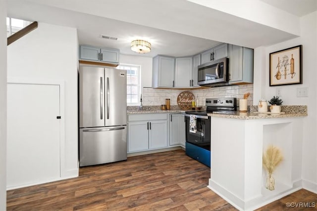 kitchen with dark wood-type flooring, backsplash, appliances with stainless steel finishes, and gray cabinetry