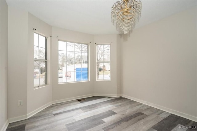 empty room with hardwood / wood-style flooring and an inviting chandelier