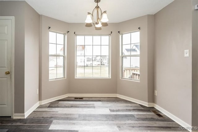 unfurnished dining area featuring plenty of natural light, dark hardwood / wood-style floors, and an inviting chandelier