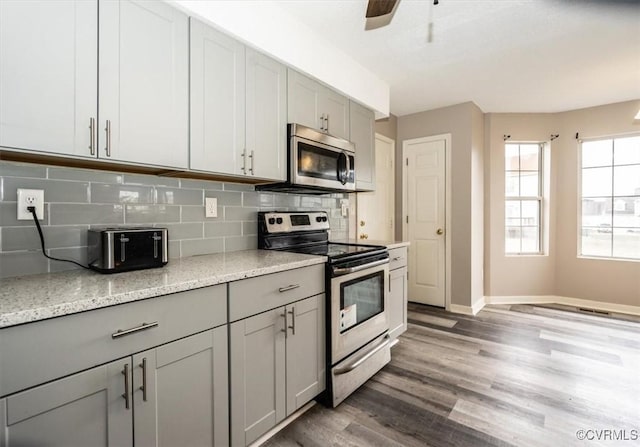 kitchen with tasteful backsplash, gray cabinetry, light stone counters, dark hardwood / wood-style floors, and stainless steel appliances