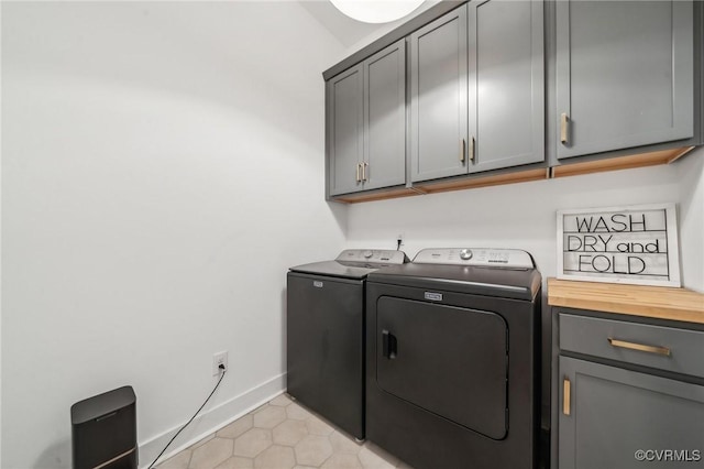 washroom featuring light tile patterned floors, washing machine and dryer, cabinet space, and baseboards