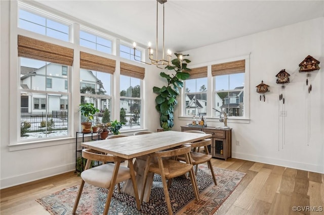 dining room featuring light wood-style floors, plenty of natural light, baseboards, and a notable chandelier