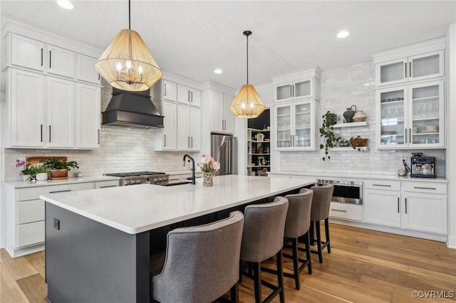 kitchen featuring white cabinets, glass insert cabinets, light countertops, and an island with sink