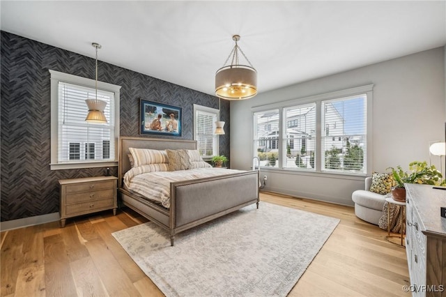 bedroom featuring light wood-type flooring, wallpapered walls, an accent wall, and baseboards