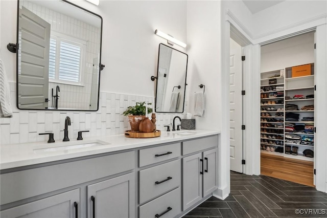 full bath featuring double vanity, parquet flooring, a sink, and decorative backsplash