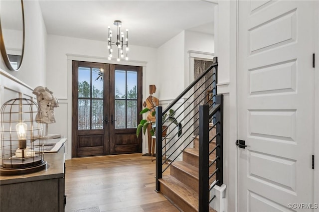 foyer with stairs, french doors, a notable chandelier, and light wood-style floors