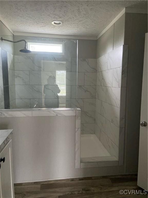 bathroom with hardwood / wood-style flooring, tiled shower, a textured ceiling, vanity, and ornamental molding