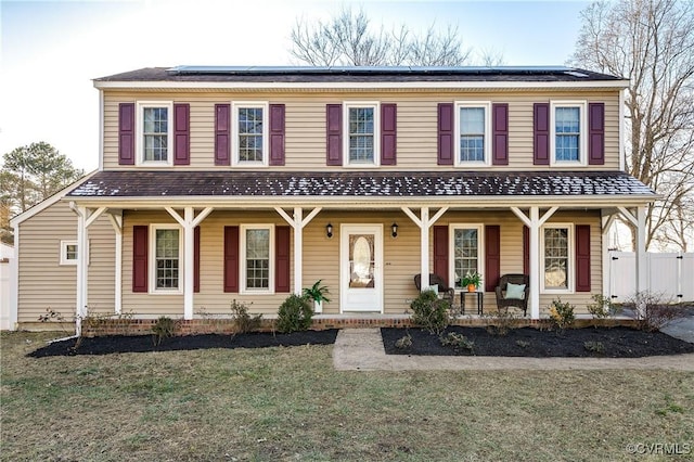 view of front of house featuring covered porch, a front yard, and solar panels