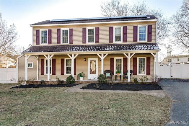 view of front of house with covered porch, a front yard, and solar panels