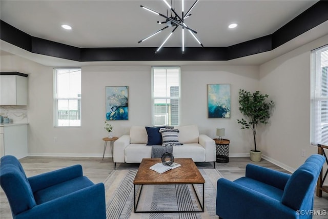 living room with light hardwood / wood-style floors, an inviting chandelier, a wealth of natural light, and a raised ceiling