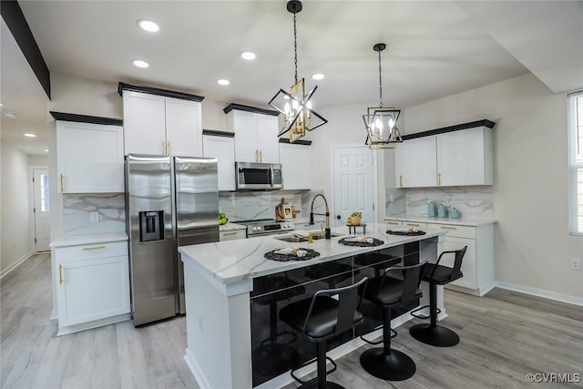 kitchen featuring hanging light fixtures, appliances with stainless steel finishes, white cabinets, light stone countertops, and a center island with sink