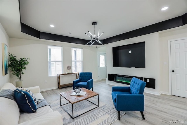 living room featuring a chandelier, light hardwood / wood-style flooring, and a raised ceiling