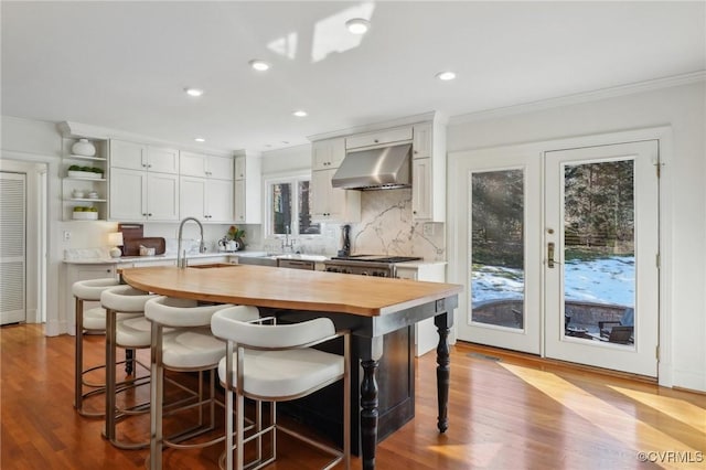 kitchen with a center island with sink, white cabinets, ventilation hood, and butcher block counters