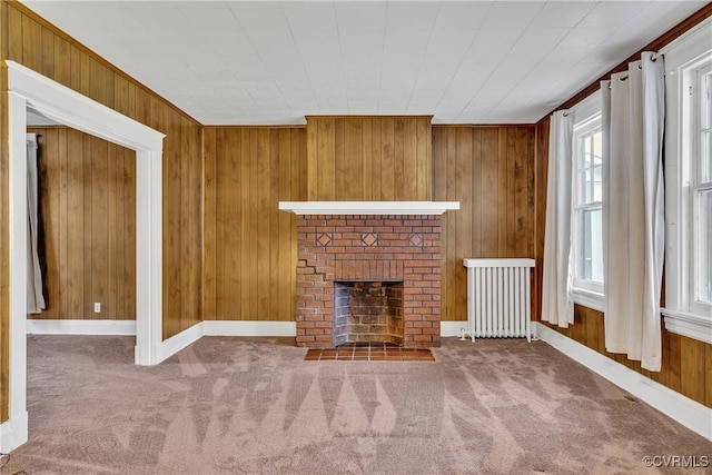 unfurnished living room featuring a fireplace, radiator heating unit, carpet flooring, and wood walls