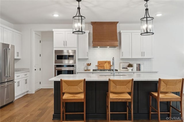 kitchen featuring white cabinets, high end refrigerator, a kitchen island with sink, and premium range hood