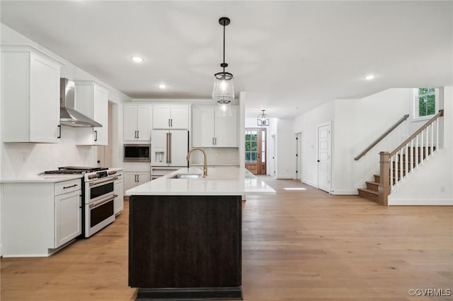 kitchen featuring decorative light fixtures, wall chimney range hood, range with two ovens, a kitchen island with sink, and stainless steel microwave