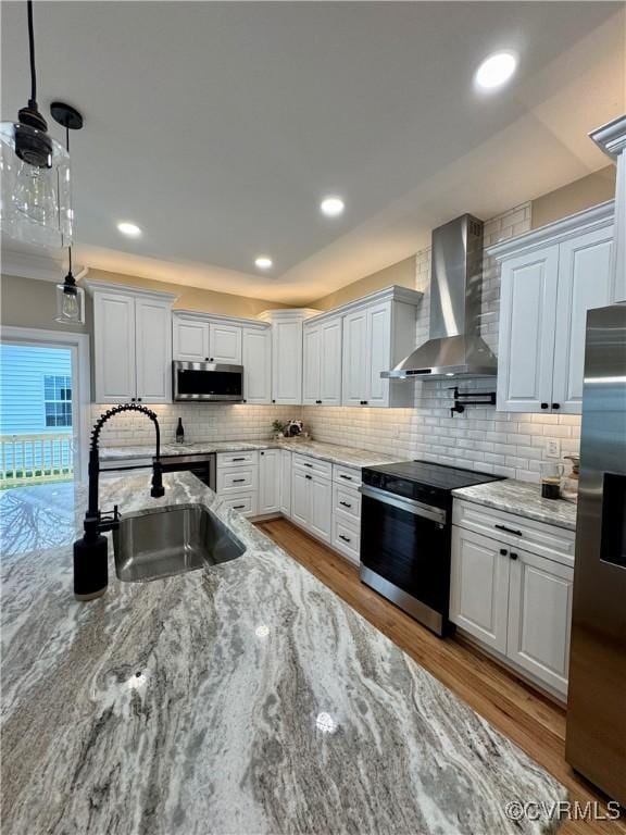 kitchen with a sink, white cabinets, appliances with stainless steel finishes, wall chimney exhaust hood, and decorative light fixtures