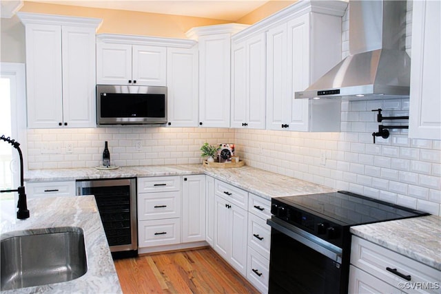 kitchen featuring beverage cooler, electric range, white cabinets, wall chimney range hood, and stainless steel microwave