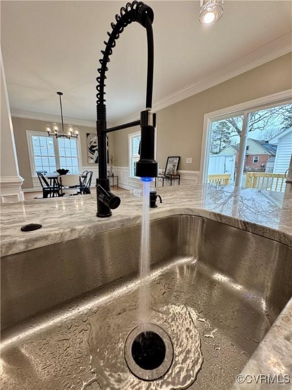 details with light stone counters, a wainscoted wall, a sink, hanging light fixtures, and ornamental molding