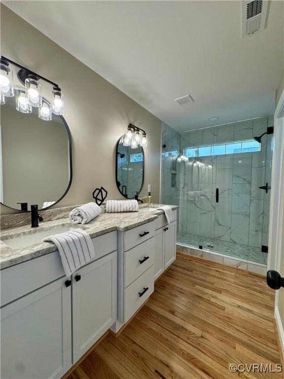 bathroom with double vanity, a shower stall, visible vents, and wood finished floors