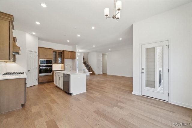 kitchen featuring appliances with stainless steel finishes, a kitchen island with sink, decorative light fixtures, light hardwood / wood-style flooring, and an inviting chandelier