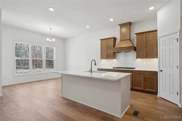 kitchen featuring pendant lighting, light hardwood / wood-style flooring, custom range hood, sink, and an island with sink