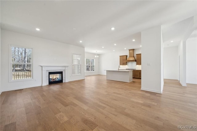 unfurnished living room featuring sink, light hardwood / wood-style floors, and a wealth of natural light