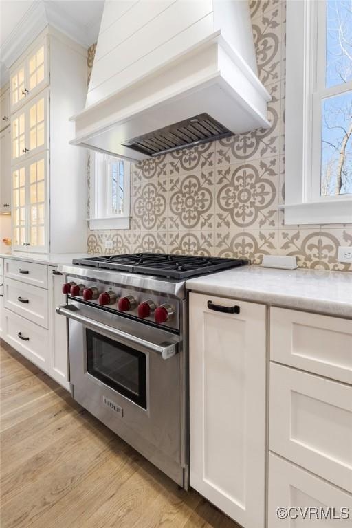 kitchen with backsplash, premium stove, custom range hood, and white cabinets