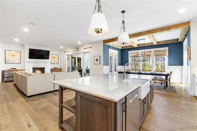 kitchen featuring pendant lighting, sink, a kitchen island with sink, light stone countertops, and light hardwood / wood-style flooring