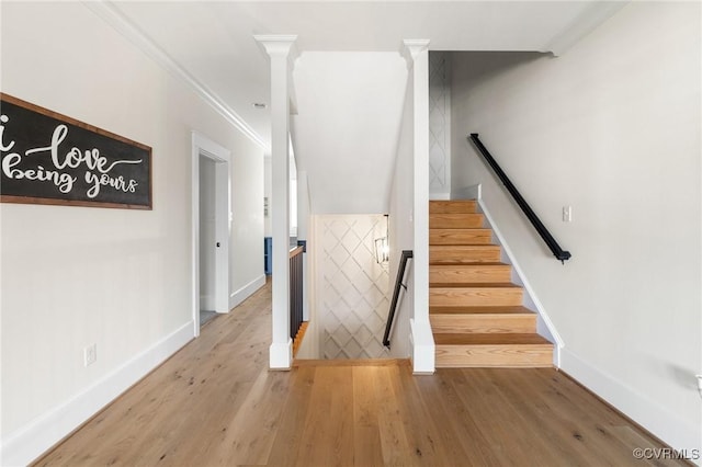 staircase featuring hardwood / wood-style flooring, crown molding, and decorative columns