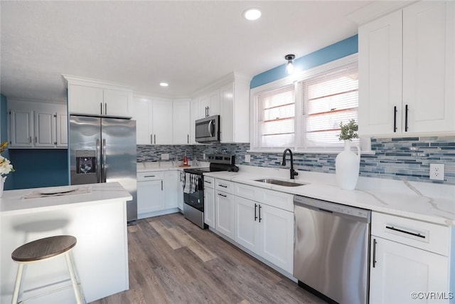 kitchen featuring sink, white cabinetry, stainless steel appliances, wood-type flooring, and light stone countertops