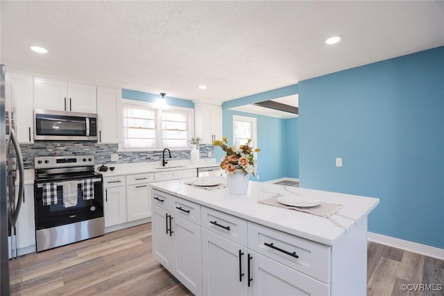 kitchen with sink, appliances with stainless steel finishes, white cabinetry, a center island, and decorative backsplash