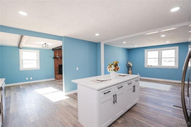 kitchen featuring light hardwood / wood-style flooring, a center island, a fireplace, a textured ceiling, and white cabinets