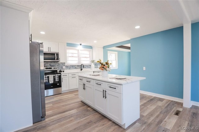 kitchen with light wood-type flooring, a center island, white cabinets, and appliances with stainless steel finishes