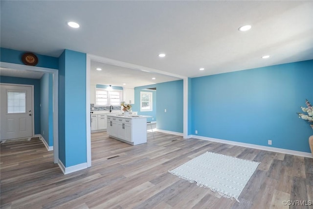 kitchen with sink, light hardwood / wood-style floors, a kitchen island, and white cabinets