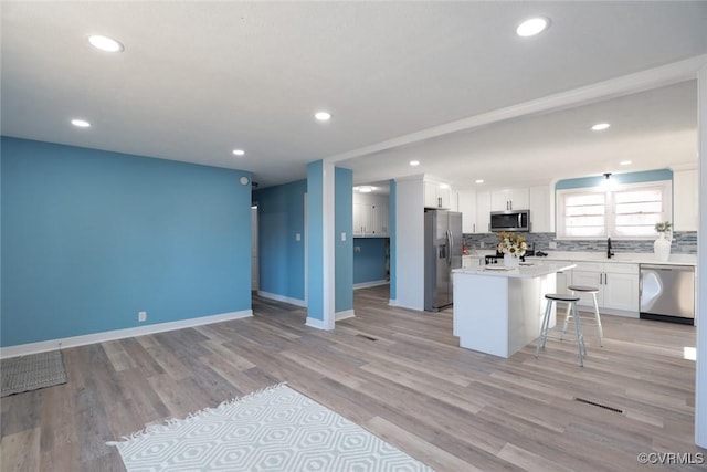 kitchen with appliances with stainless steel finishes, white cabinetry, a center island, tasteful backsplash, and a kitchen bar