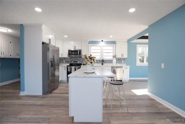 kitchen with white cabinetry, a center island, a kitchen breakfast bar, stainless steel appliances, and backsplash