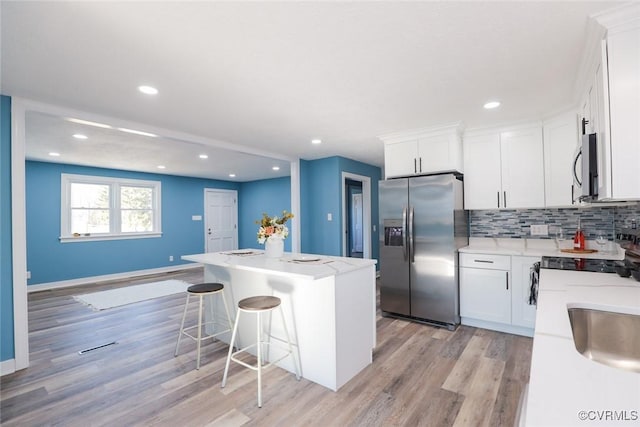 kitchen with appliances with stainless steel finishes, a center island, tasteful backsplash, white cabinets, and a kitchen bar