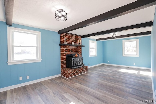 unfurnished living room with beam ceiling, a wood stove, a textured ceiling, and hardwood / wood-style flooring