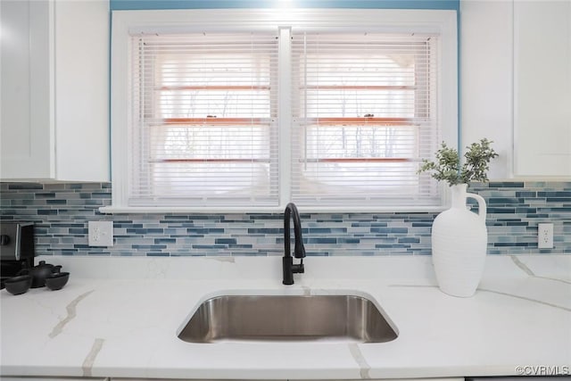 room details featuring white cabinetry, light stone countertops, sink, and decorative backsplash