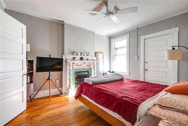 bedroom featuring hardwood / wood-style floors, ornamental molding, a tile fireplace, and ceiling fan