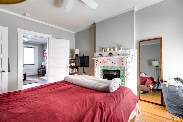 bedroom featuring a tile fireplace, wood-type flooring, lofted ceiling, ceiling fan, and crown molding