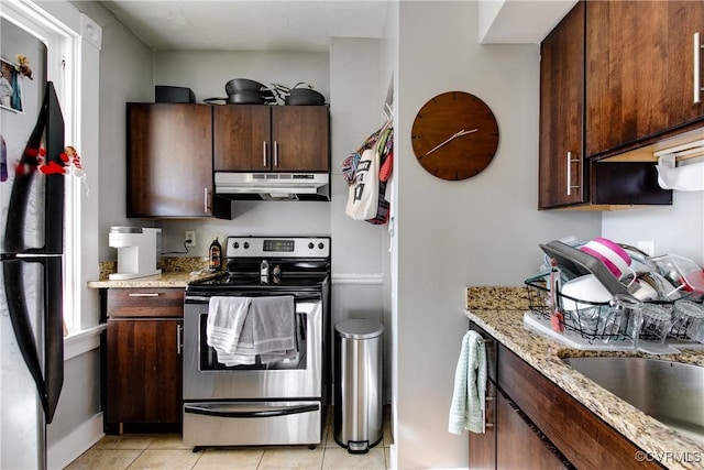 kitchen with light tile patterned flooring, dark brown cabinetry, light stone counters, black refrigerator, and stainless steel electric stove