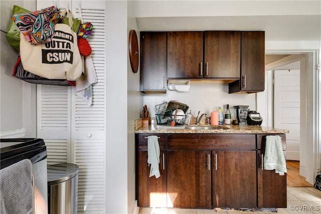 bar with dark brown cabinetry, sink, light tile patterned floors, and light stone counters