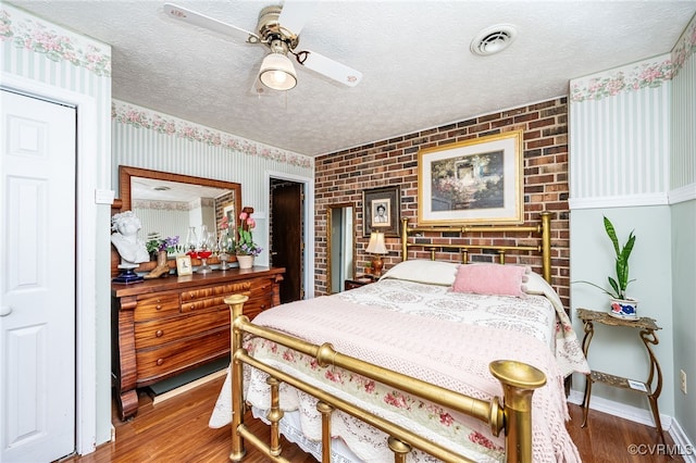 bedroom with ceiling fan, wood-type flooring, brick wall, and a textured ceiling