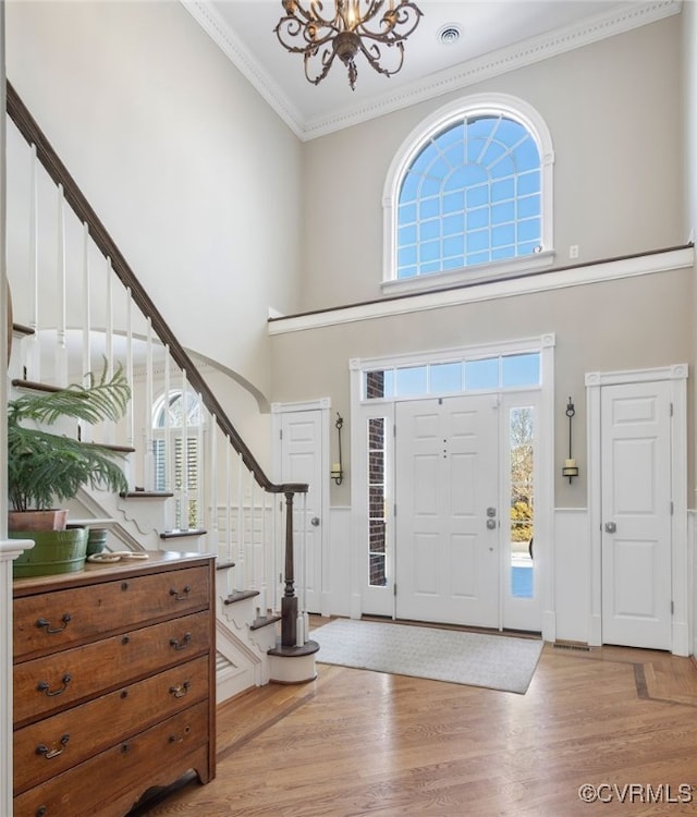 entrance foyer with crown molding, a towering ceiling, light hardwood / wood-style floors, and a healthy amount of sunlight