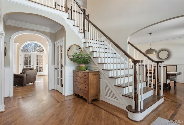 staircase with french doors, ornamental molding, hardwood / wood-style floors, and a high ceiling